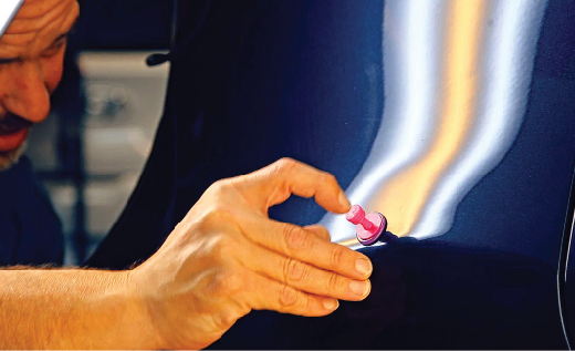 A man is applying Master Glue tab to a dent on a car.