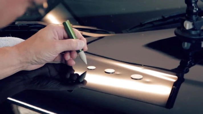 A person is using a pen to mark off dents on a car's hood as part of the Master Glue Pull Course.