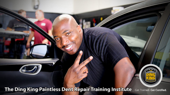 A man smiles and holds up a peace sign while leaning out of a car door in an auto repair shop. Text reads "The Ding King Paintless Dent Repair Training Institute" and "Get Trained. Get Certified in Hail Repair.