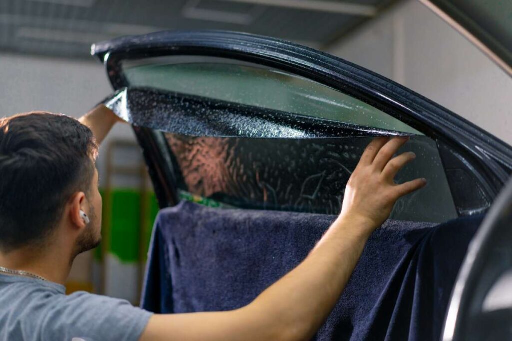 In the cozy confines of a garage, a skilled technician expertly applies window tint film to a car door, ensuring seamless precision. Alongside, the robust PPF windshield protection film awaits its turn, promising to safeguard against scratches and road debris.